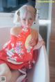 A woman in a red kimono sitting in a bathtub holding a fan.