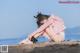 A woman in a pink jacket and white panties sitting on a beach.