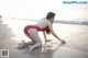 A woman in a red bathing suit crouching on the beach.