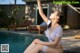 A woman in a white bikini sitting by a swimming pool.