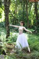 A woman in a white tutu is standing in the woods.