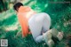 A woman in white leggings and an orange hoodie crouching down in the grass.